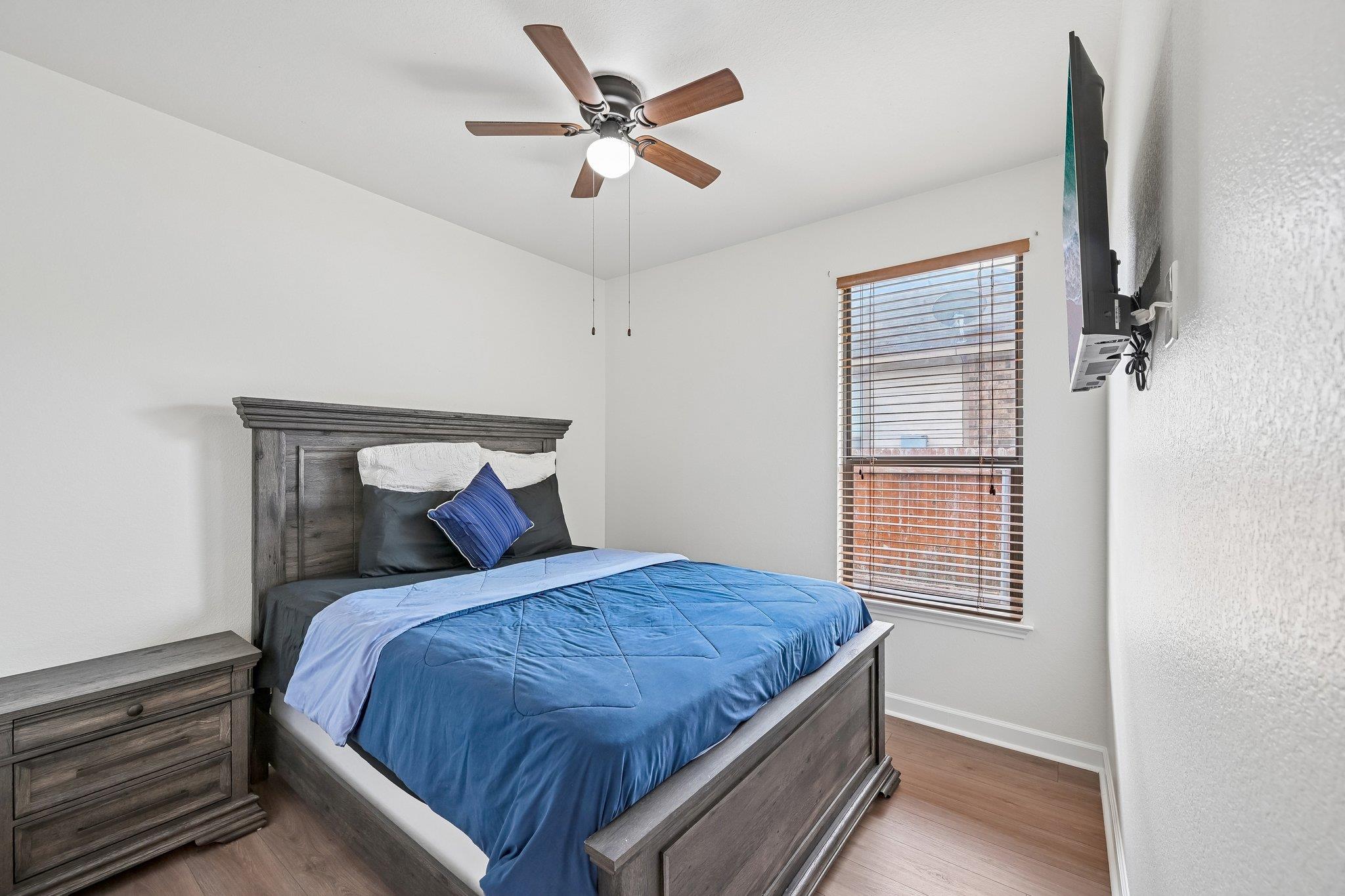 Furnished bedroom with blue bedding, dark wood furniture, a ceiling fan, and a window with blinds.