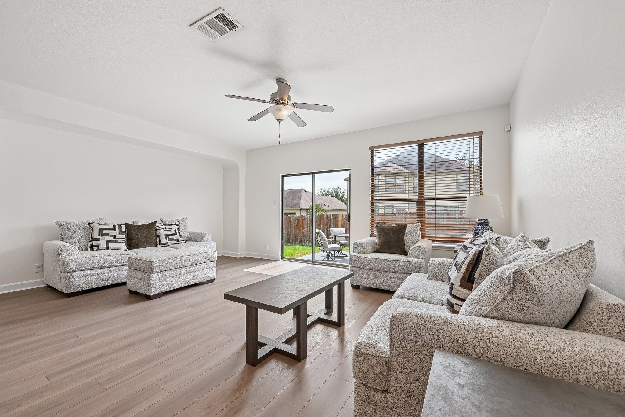 Furnished living room with gray sofas, light wood flooring, and sliding doors to a fenced backyard.