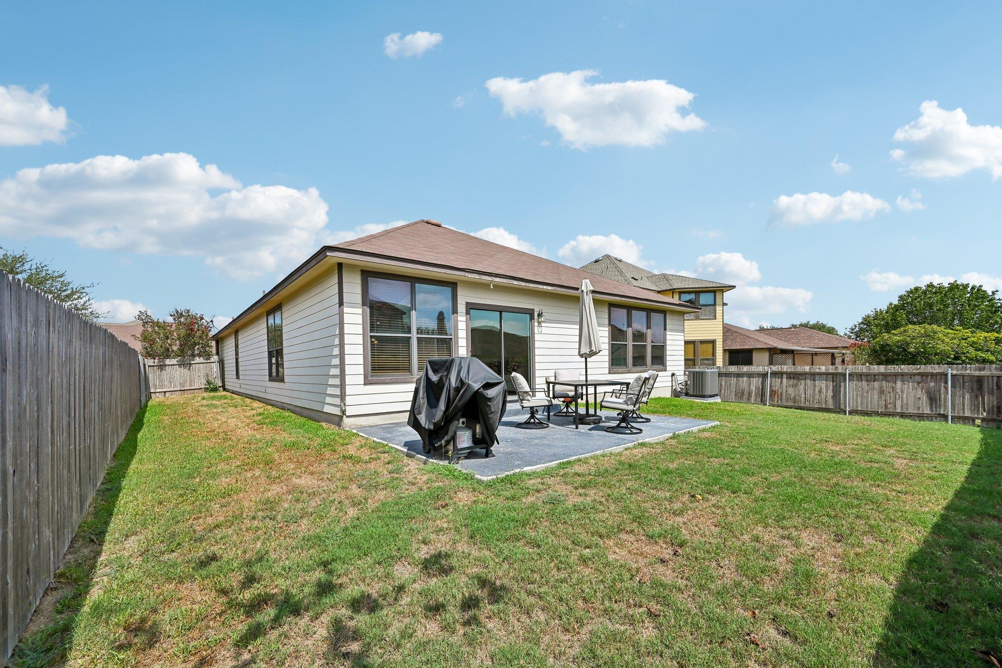 Rear of a single-story home with a fenced yard and patio seating beside a covered grill.