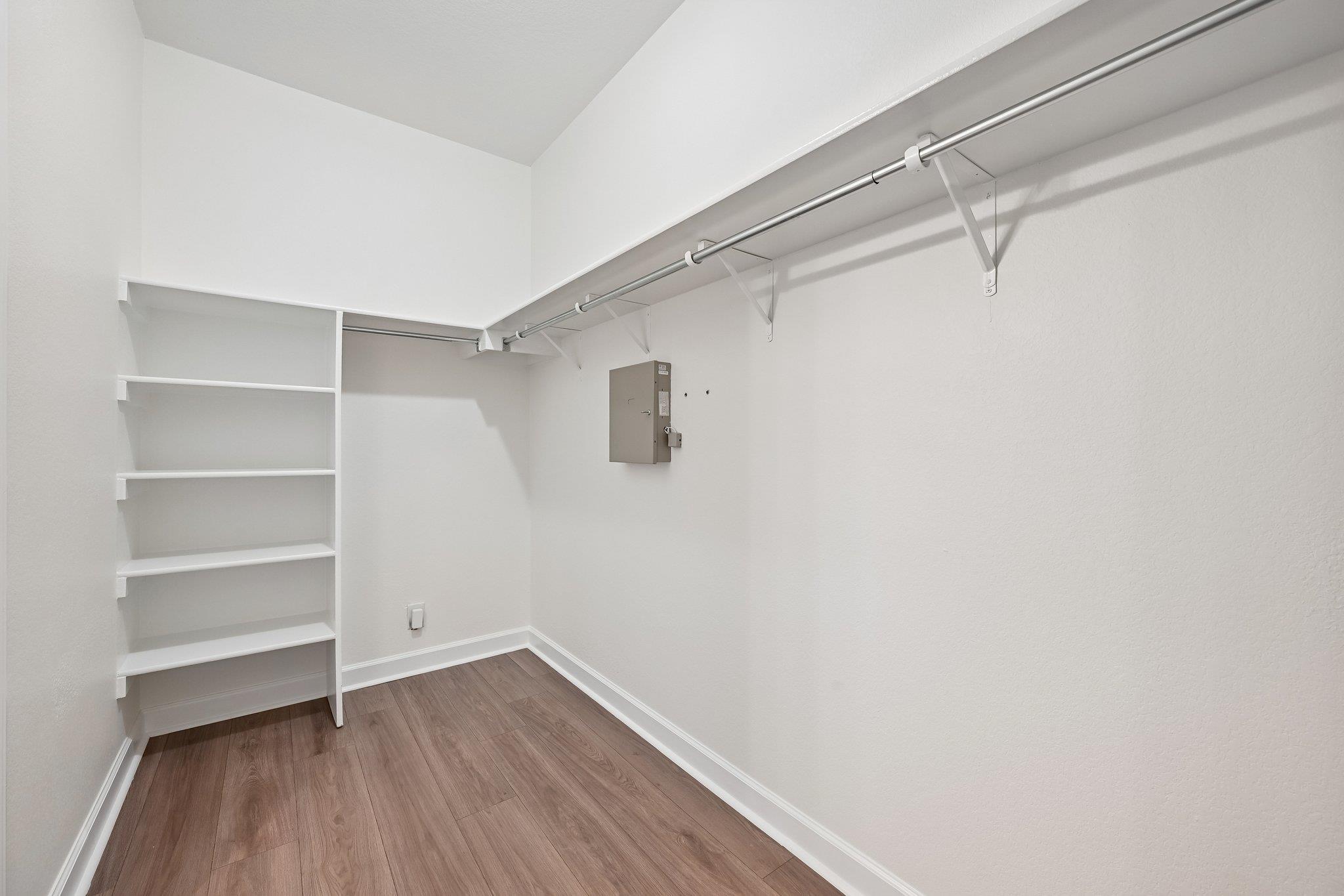 Walk-in closet with built-in shelves, hanging rods, and wood-look flooring.