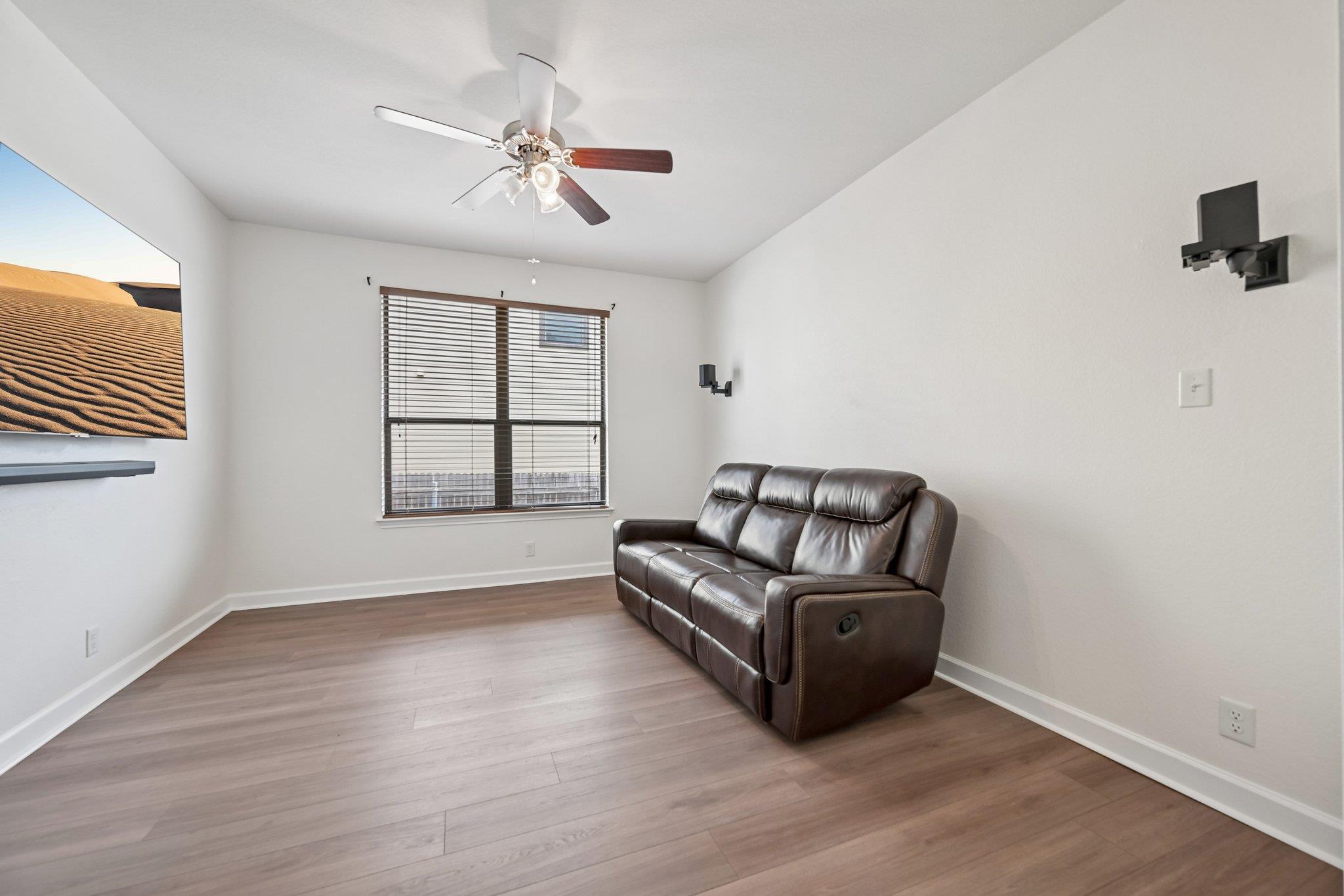 Living room with a dark leather reclining sofa, ceiling fan, and window with blinds.