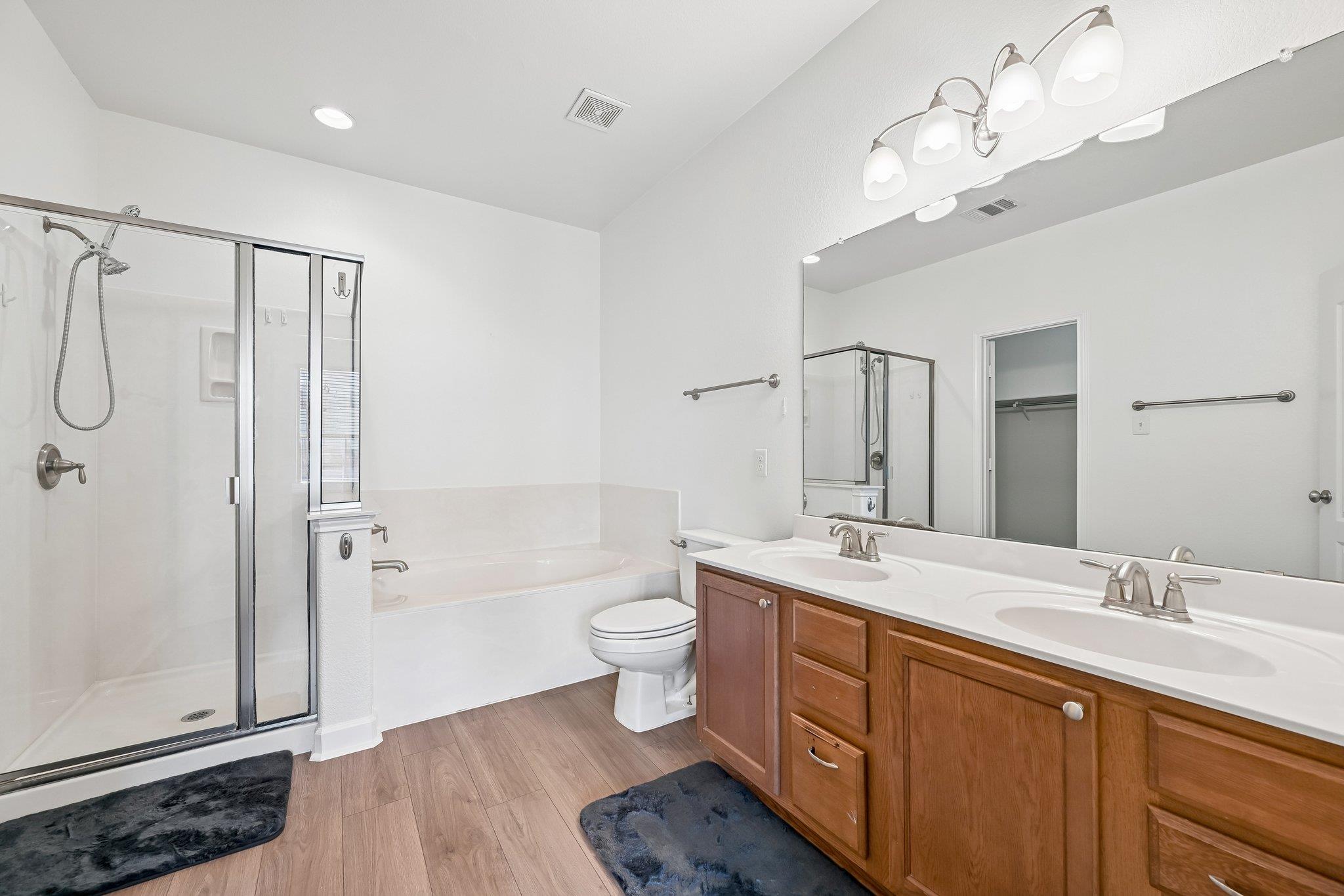 Bathroom with glass shower, built-in tub, and double-sink wood vanity.