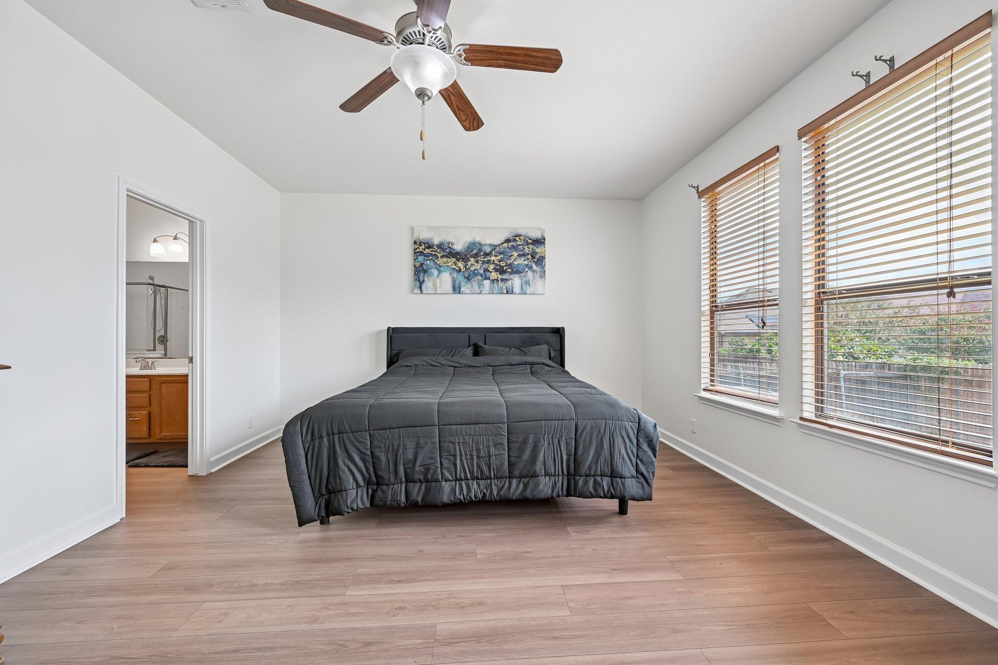 Bedroom with a dark gray bed, abstract wall art, and two sunlit windows with wooden blinds.