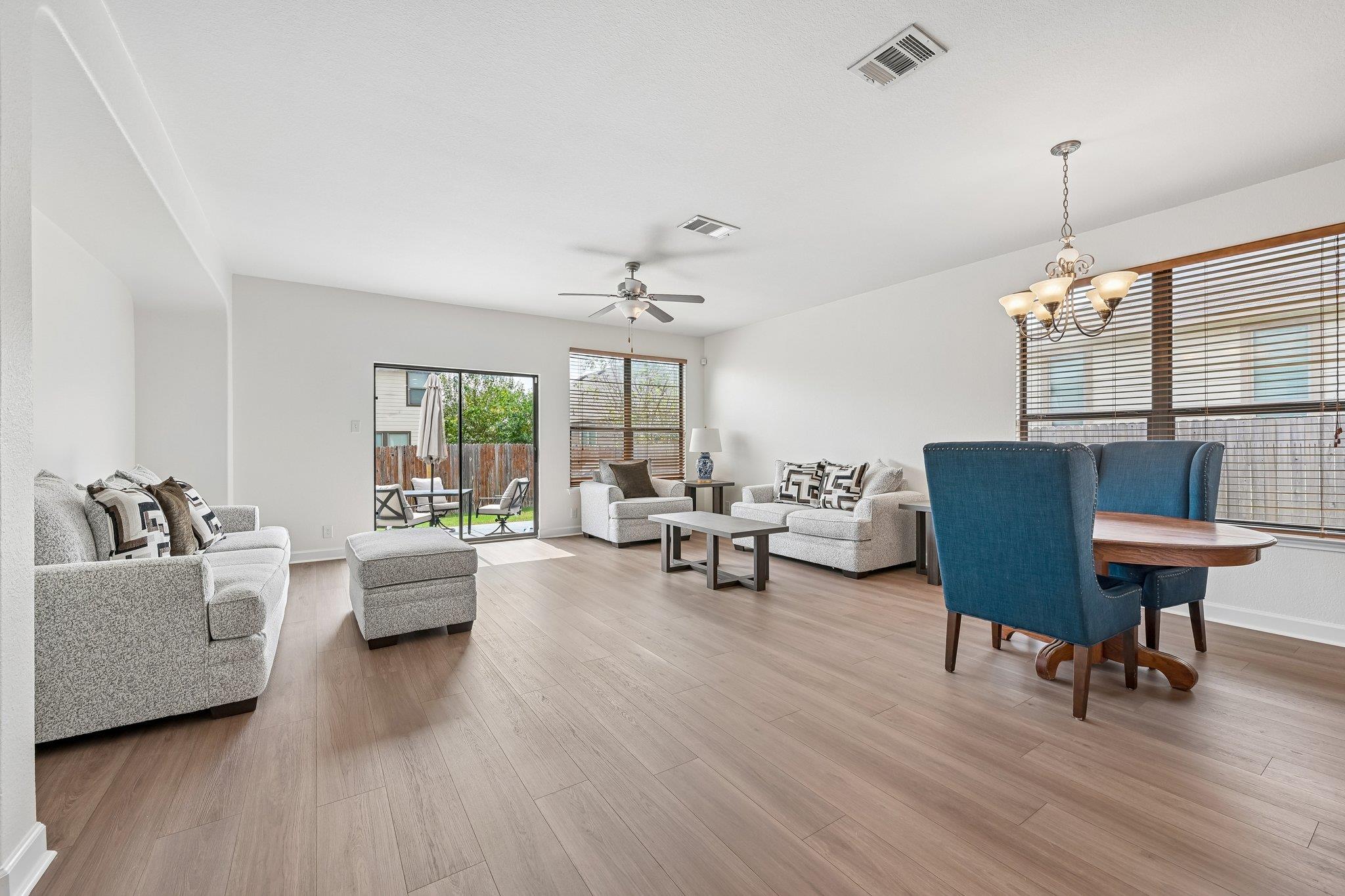 Open-plan living and dining room with gray sofas, blue dining chairs, and sliding glass doors to a patio.