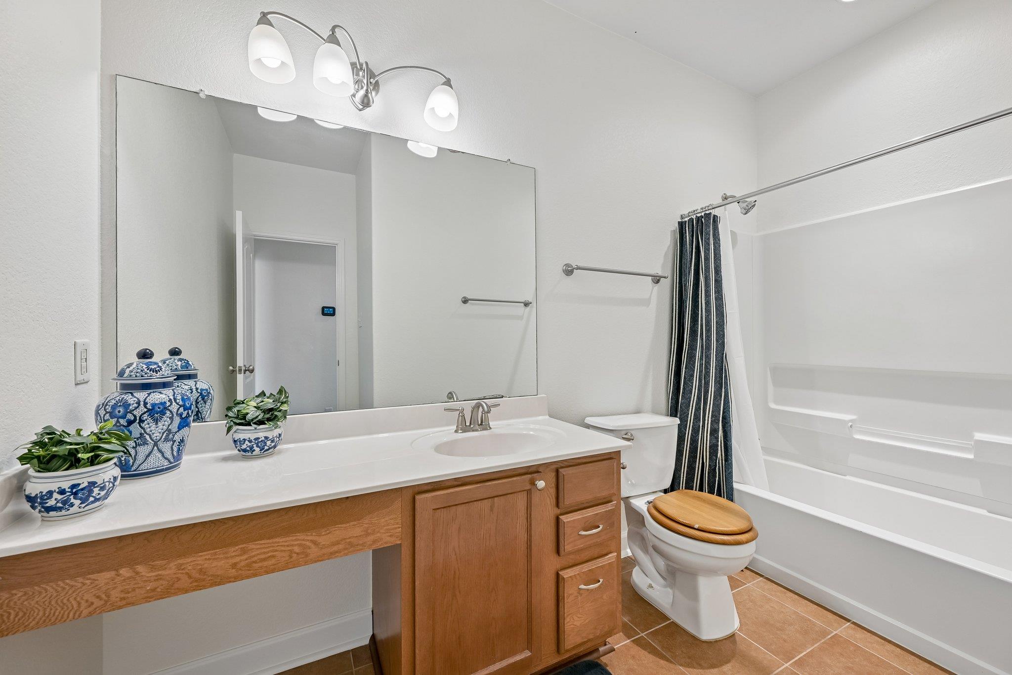 Bathroom with a wood vanity, large mirror, toilet, and white tub-shower with a dark striped curtain.