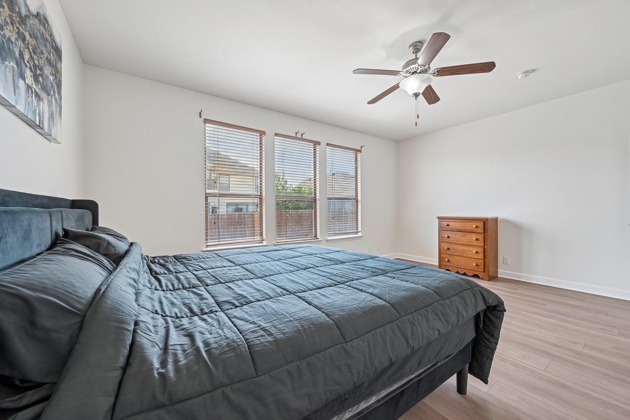 Bedroom with a large dark quilted bed, three blinded windows, and a wooden dresser.