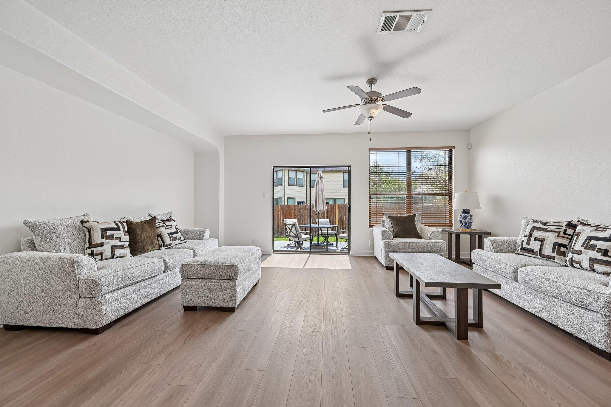 Furnished living room with light gray sofas and a sliding glass door to a fenced patio.