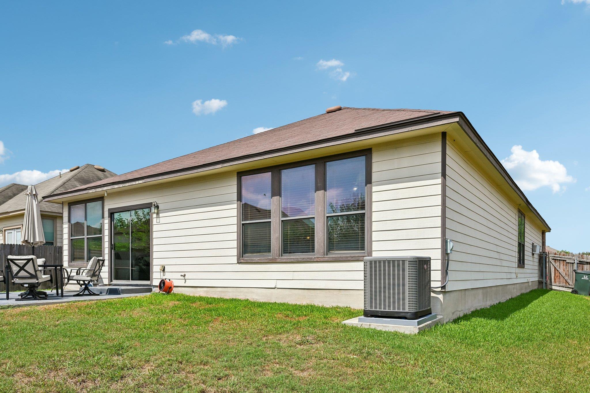 Rear exterior of a single-story home with a small patio, outdoor seating, and a broad lawn.