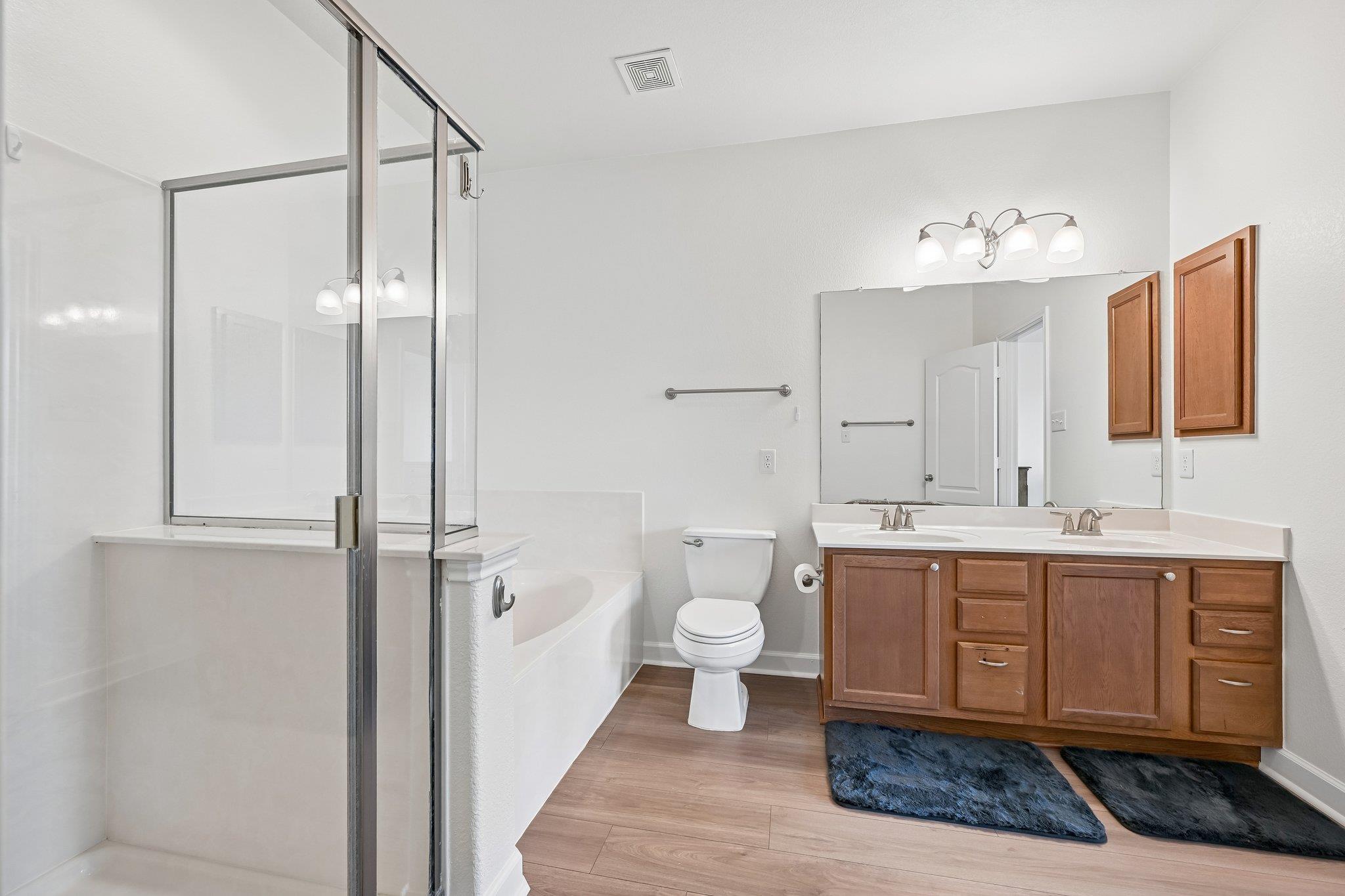 Bathroom with glass shower and tub, toilet, and wood double vanity with two sinks.