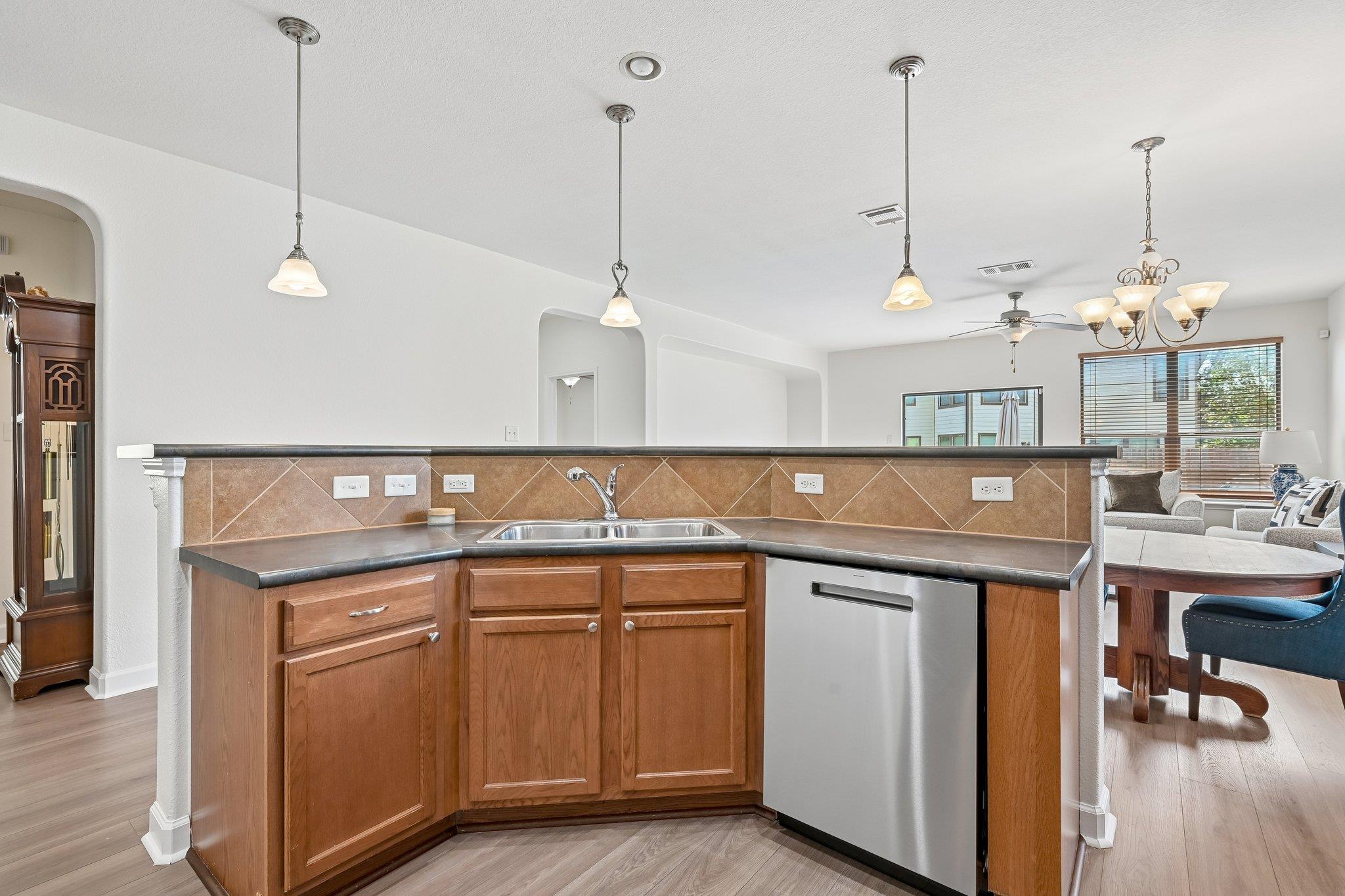 Kitchen breakfast bar with wood cabinets and stainless dishwasher, opening to a furnished dining and living area.