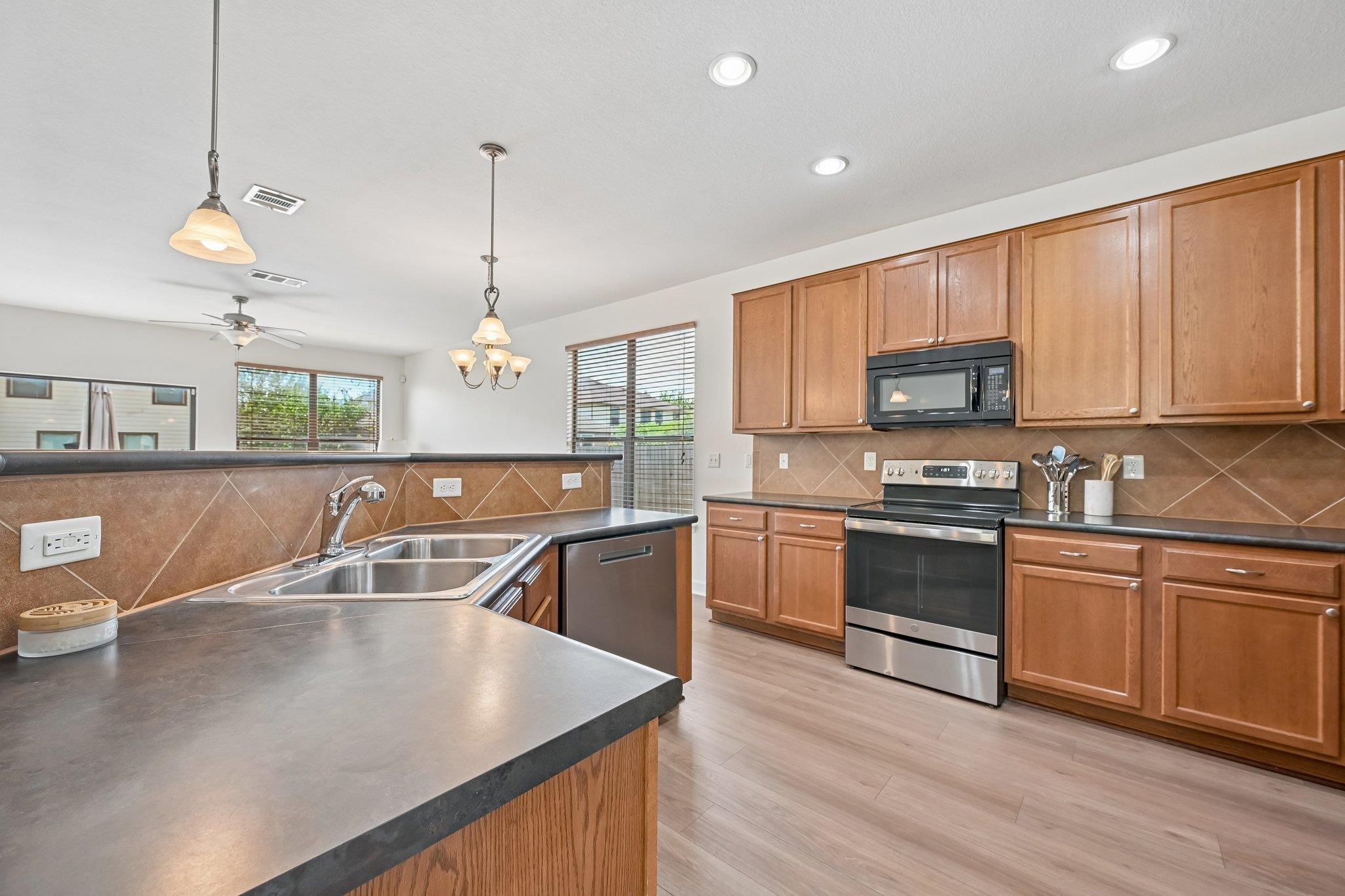 Kitchen with wood cabinetry, a large sink island, dark counters, and stainless steel appliances.