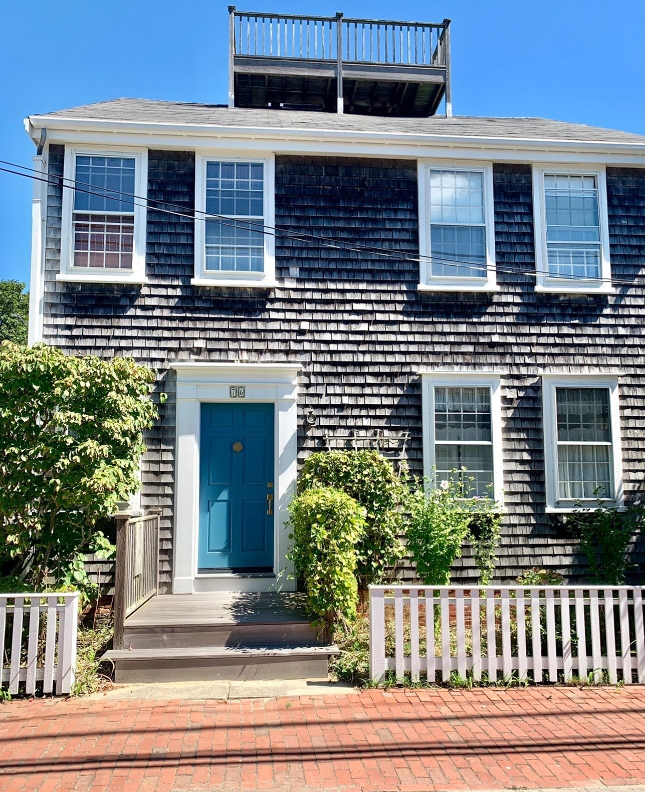 Dark shingle-sided home with a bright blue front door, white trim, and rooftop deck.