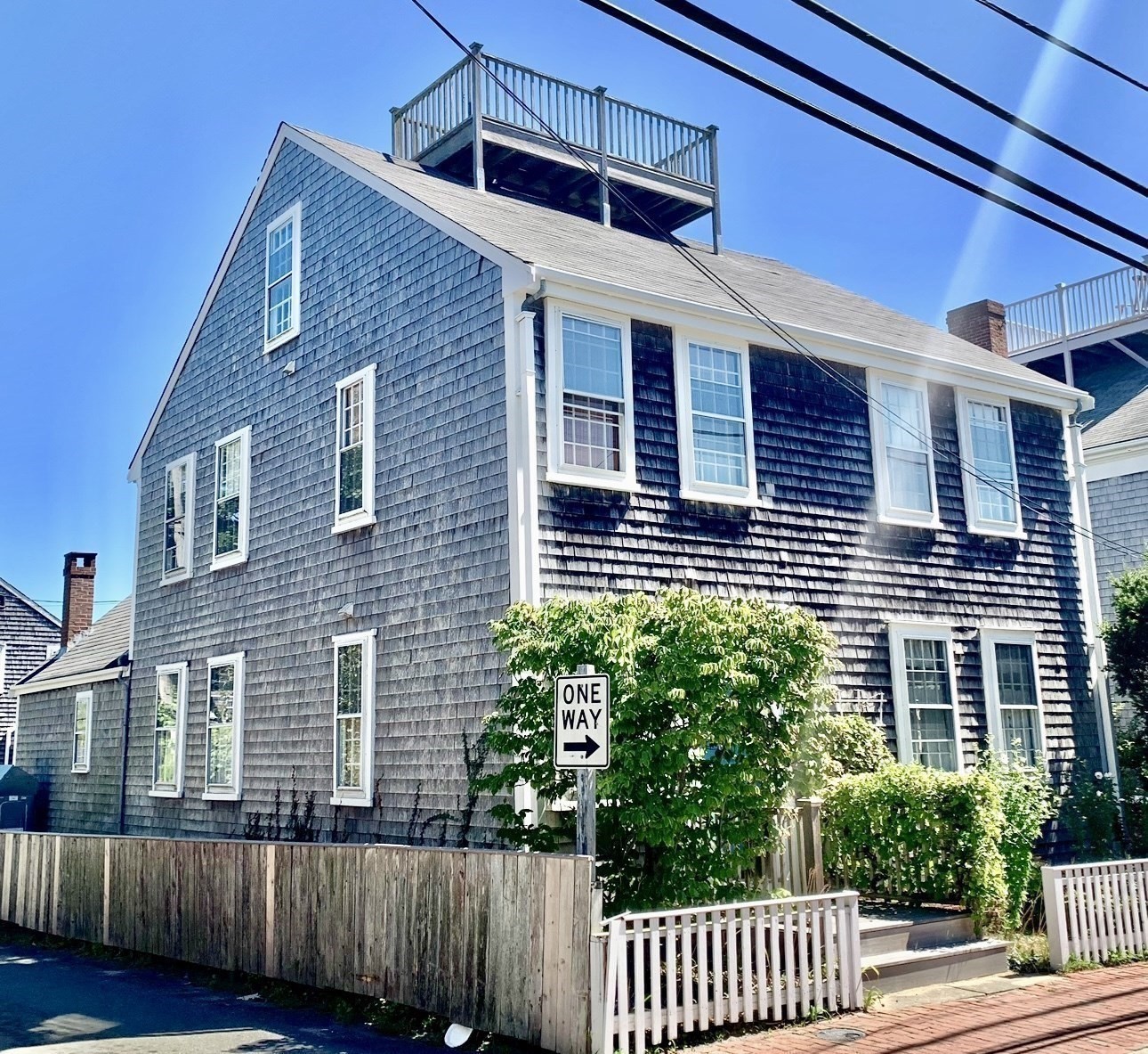 Gray shingle-sided house with white trim, rooftop deck, and fenced garden entrance.