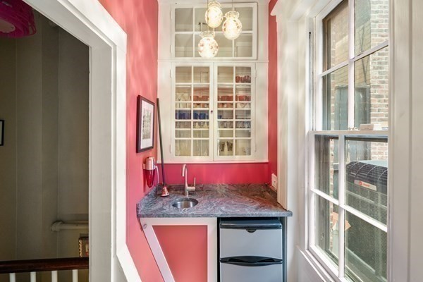 Compact kitchen nook with pink walls, glass-front cabinets, and a marble-patterned counter.