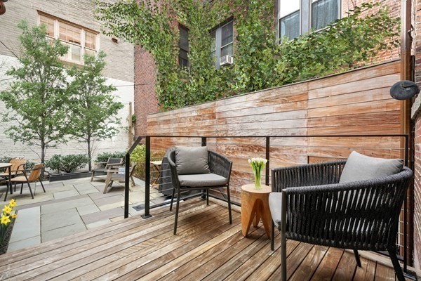 Outdoor patio with a wooden deck, lounge chairs, a privacy screen, and leafy courtyard plants.