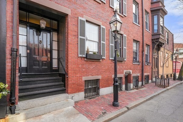 Red-brick townhouse facade with a black entry door, stone stoop, and sidewalk.