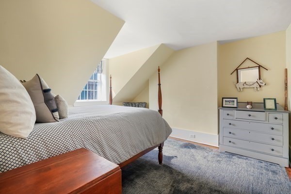 Attic bedroom with a low sloped ceiling, patterned bedcover, and gray dresser.