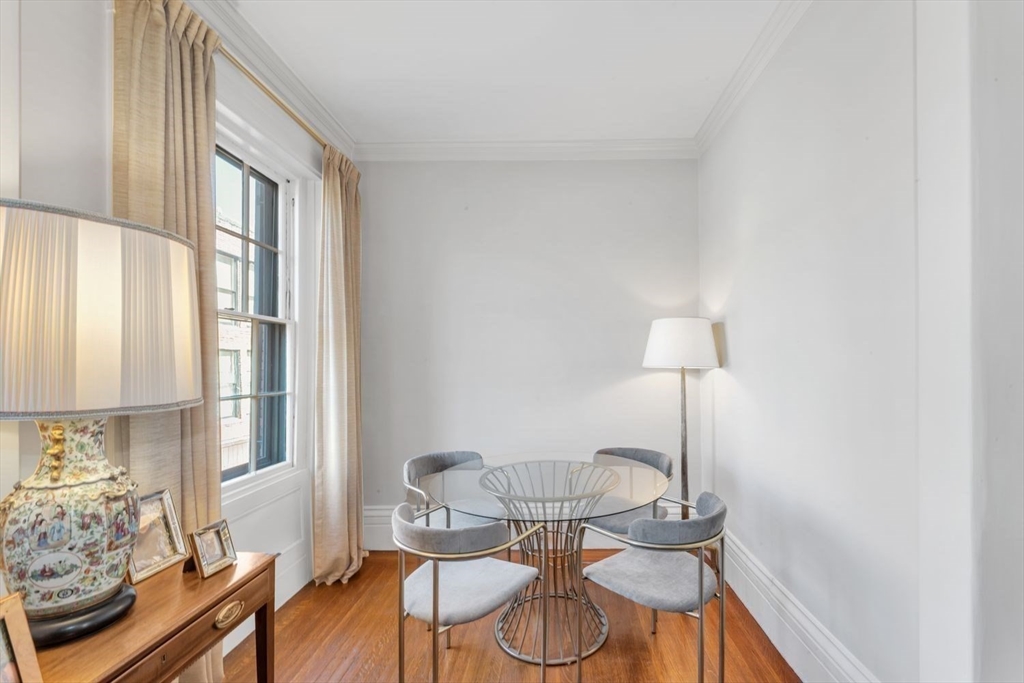 Dining area with a round glass table, upholstered chairs, tall curtained windows, and hardwood floors.