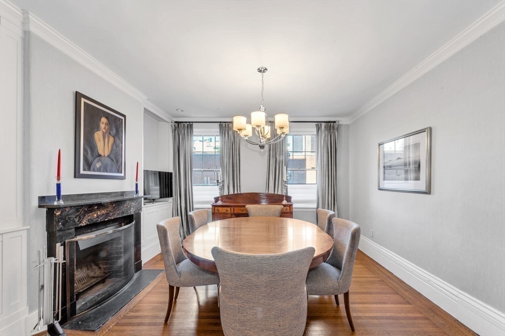 Dining room with a round wooden table, marble fireplace, and tall curtained windows.