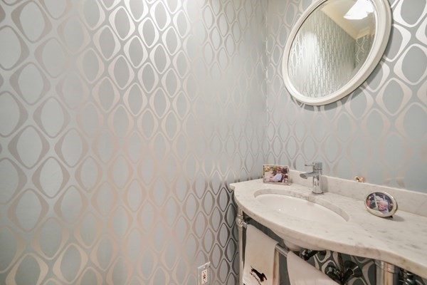 Bathroom vanity with a marble countertop, oval mirror, and pale geometric wallpaper.