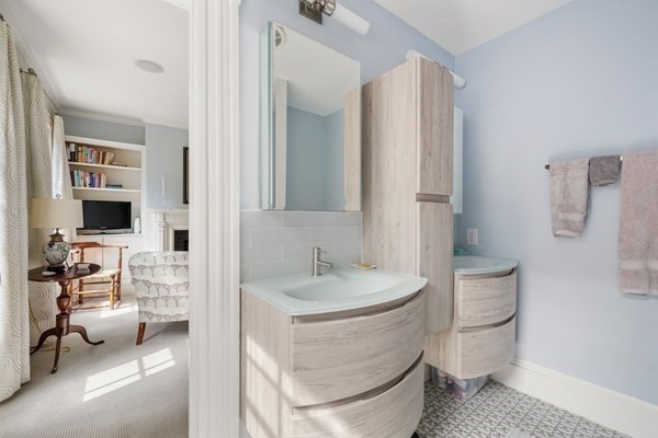 Bathroom with two pale wood vanities and vessel sinks beside a doorway to a sitting room.