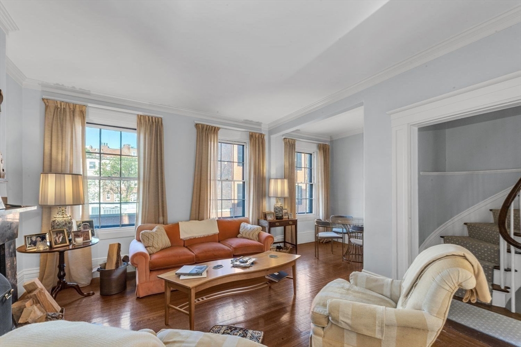Living room with an orange sofa, tall curtained windows, and a staircase.