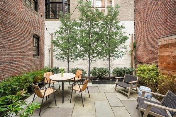 Enclosed brick courtyard patio with outdoor dining and lounge seating among small trees.