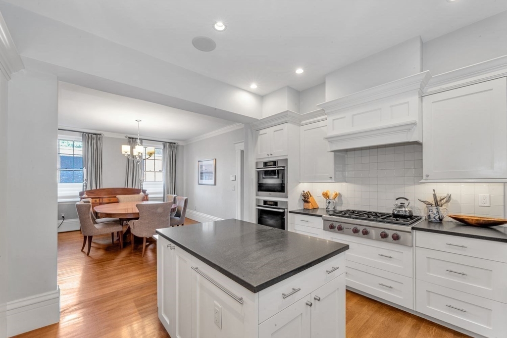 White kitchen with a dark stone island, gas range, and adjoining dining area with tall windows.