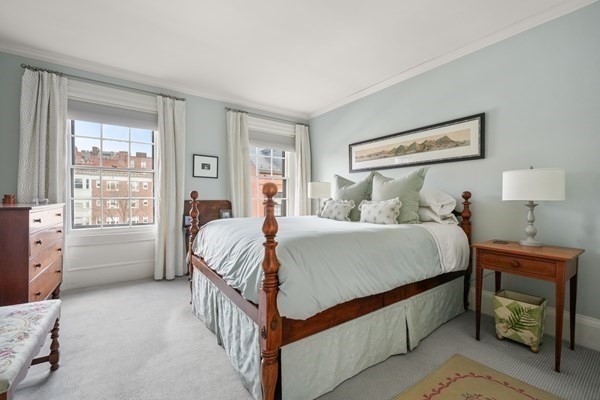 Bedroom with a wood four-poster bed and tall windows overlooking brick buildings.