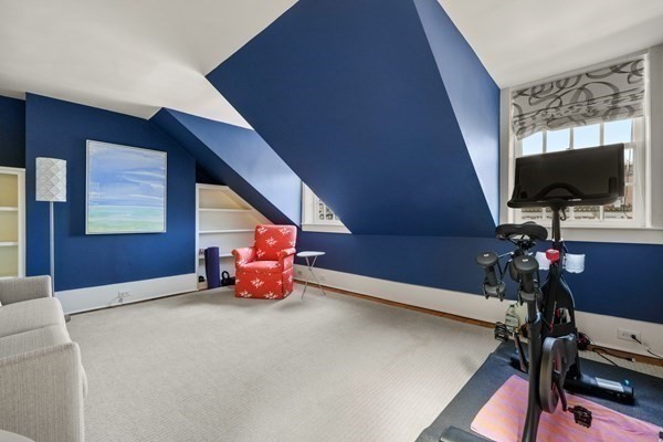 Attic room with deep blue sloped walls, a red patterned chair, and an exercise bike by the window.