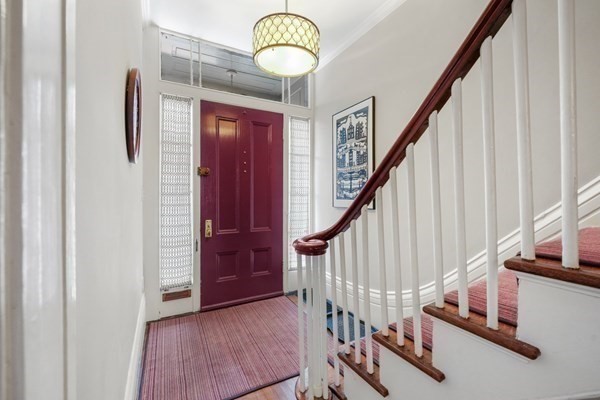 Entry hall with a red front door and white staircase with a dark wood handrail.