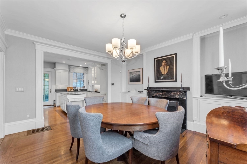 Dining room with a round wooden table, chandelier, fireplace, and adjoining kitchen.