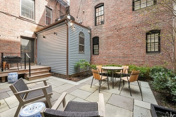 Private courtyard with brick walls, a patio dining set, lounge chairs, and wooden steps.