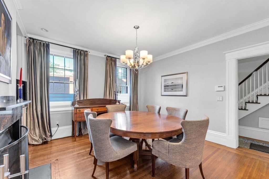 Dining room with an oval wooden table, upholstered chairs, tall windows, and a chandelier.