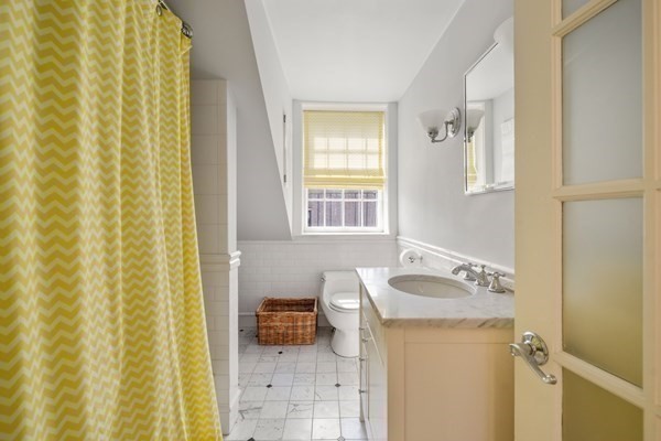 Bathroom with a yellow chevron shower curtain, marble vanity, and window.
