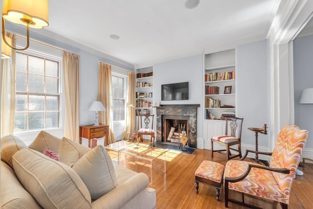 Living room with a marble fireplace, built-in bookshelves, and sunlight streaming through large windows.
