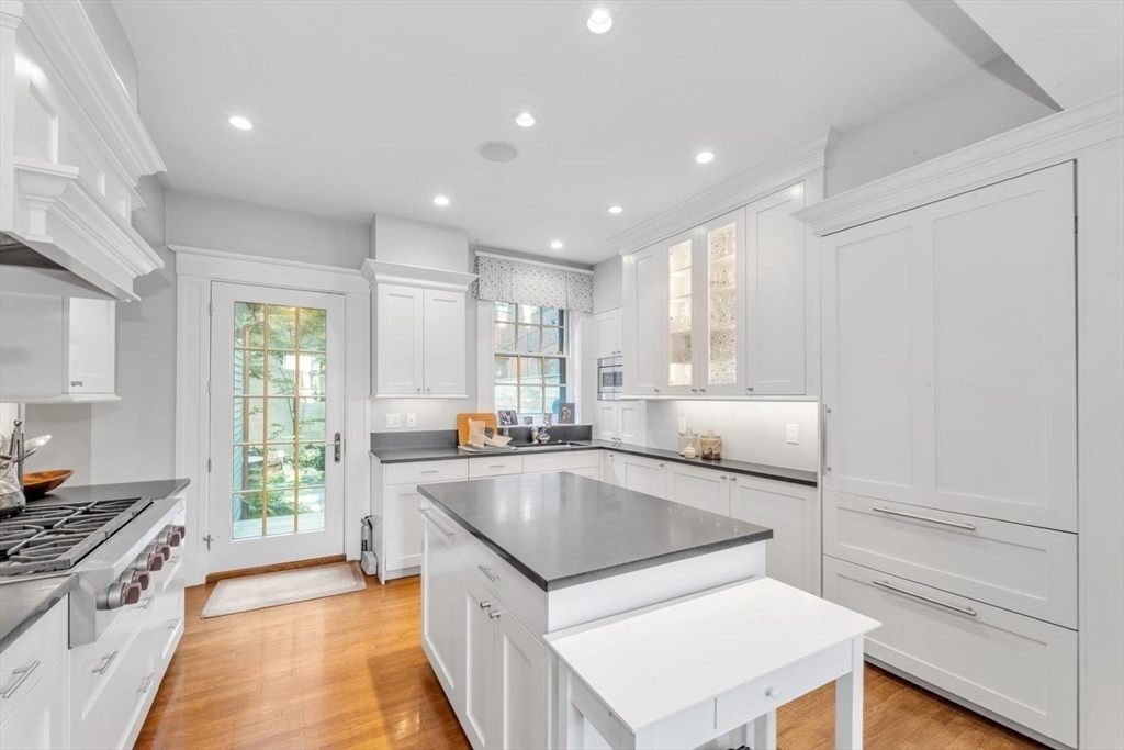 White kitchen with a gray island, stainless steel range, and glass-paneled door to greenery.