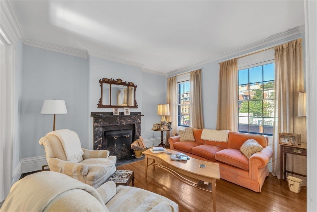 Living room with a marble fireplace, tall windows, hardwood floors, and cream and orange seating.