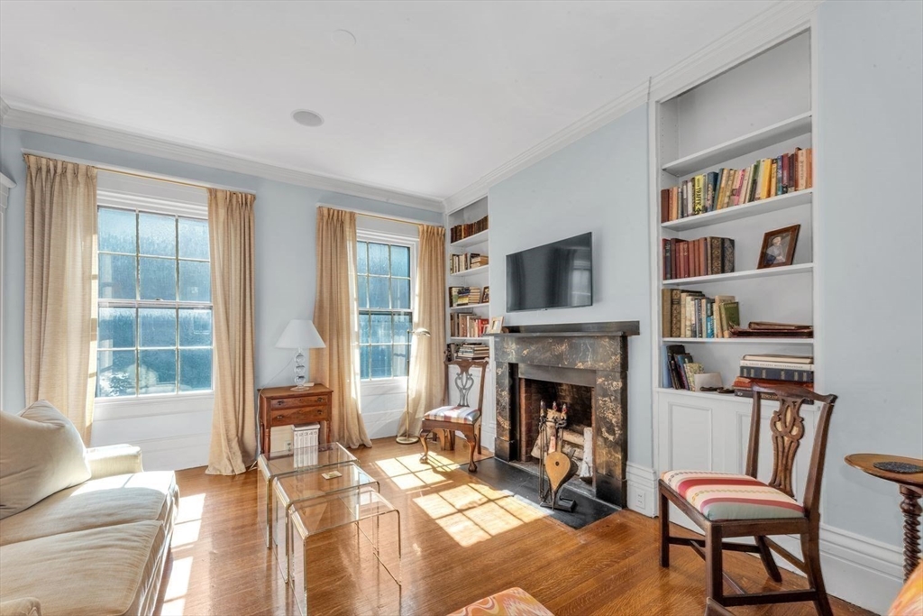 Living room with a marble fireplace, built-in bookshelves, tall sunny windows, and hardwood floors.