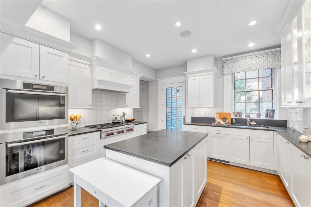 Bright white kitchen with stainless steel double ovens, a gas range, and a large gray-topped island.