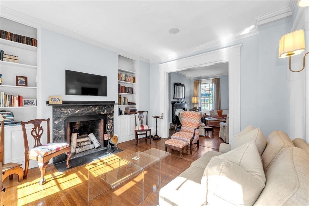 Living room with a marble fireplace, built-in bookshelves, hardwood floors, and an adjoining sitting room.