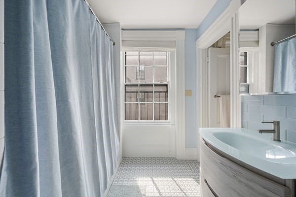 Bathroom with a pale blue shower curtain, patterned tile floor, and curved basin.