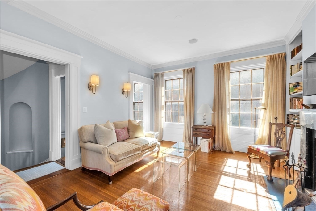 Living room with a beige sofa, tall curtained windows, hardwood floors and a glass coffee table.
