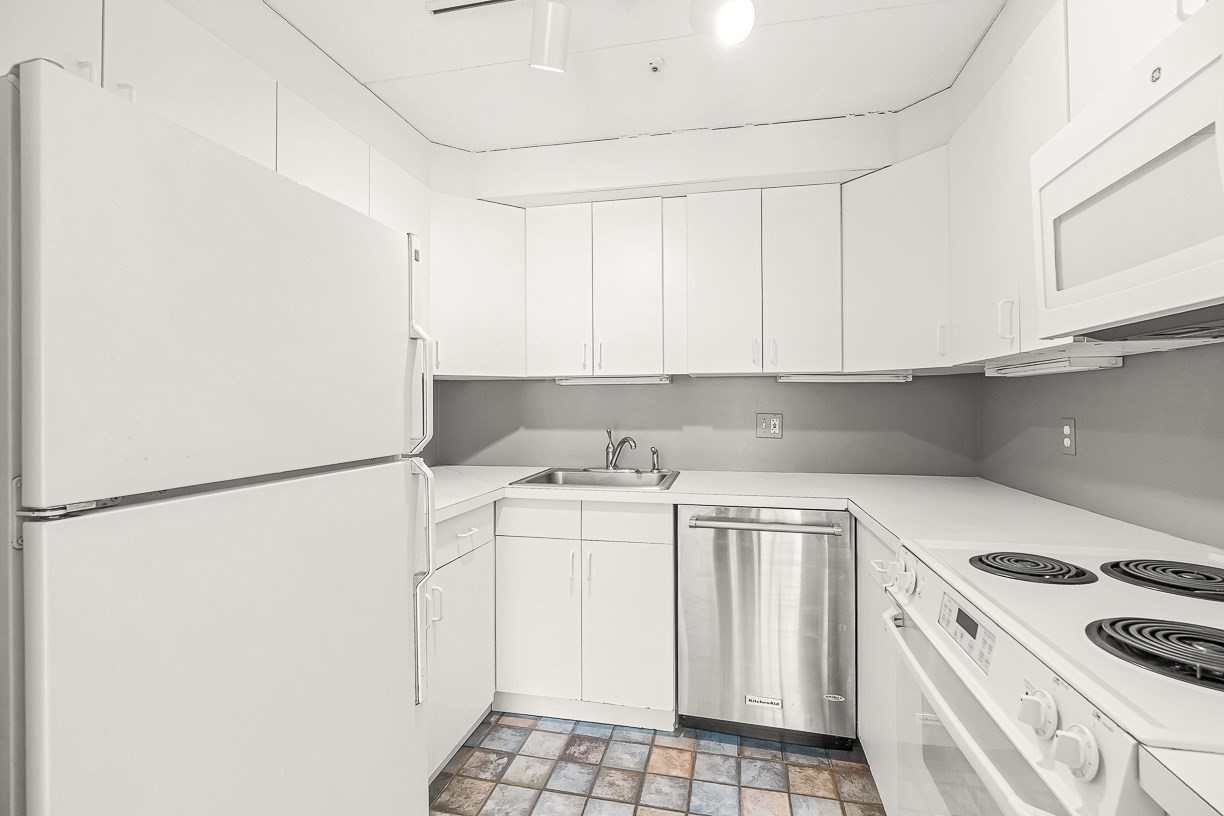 White U-shaped kitchen with stainless steel dishwasher and multicolored tile floor.