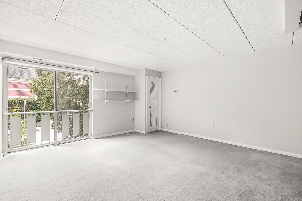 Vacant carpeted room with a sliding glass door to a balcony and wall-mounted shelves.