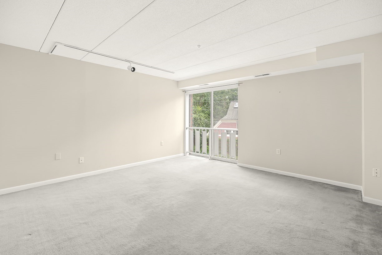 Empty carpeted room with a sliding glass door opening to a balcony.