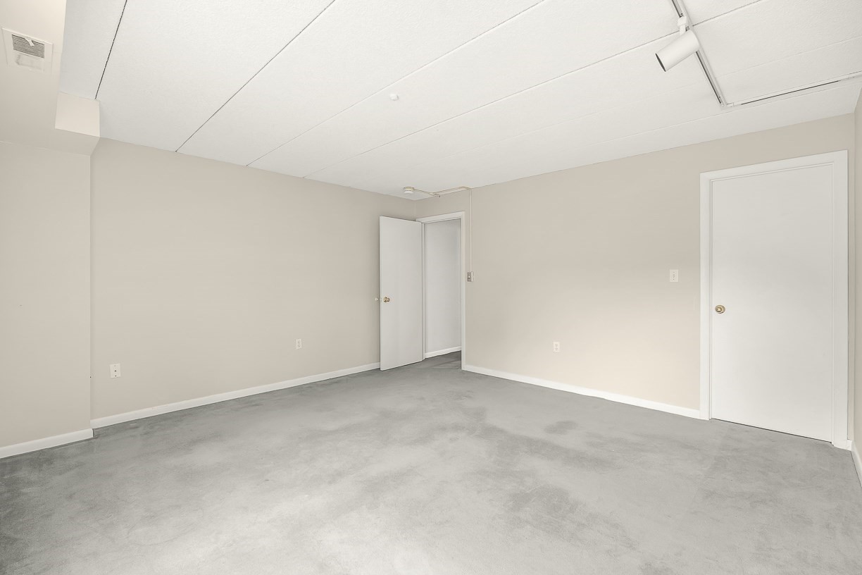 Empty carpeted room with a paneled ceiling and one open door.