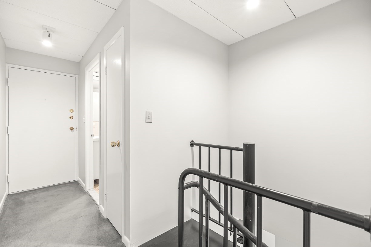 Apartment entry hall with a white front door, gray carpet, and black stair railings.