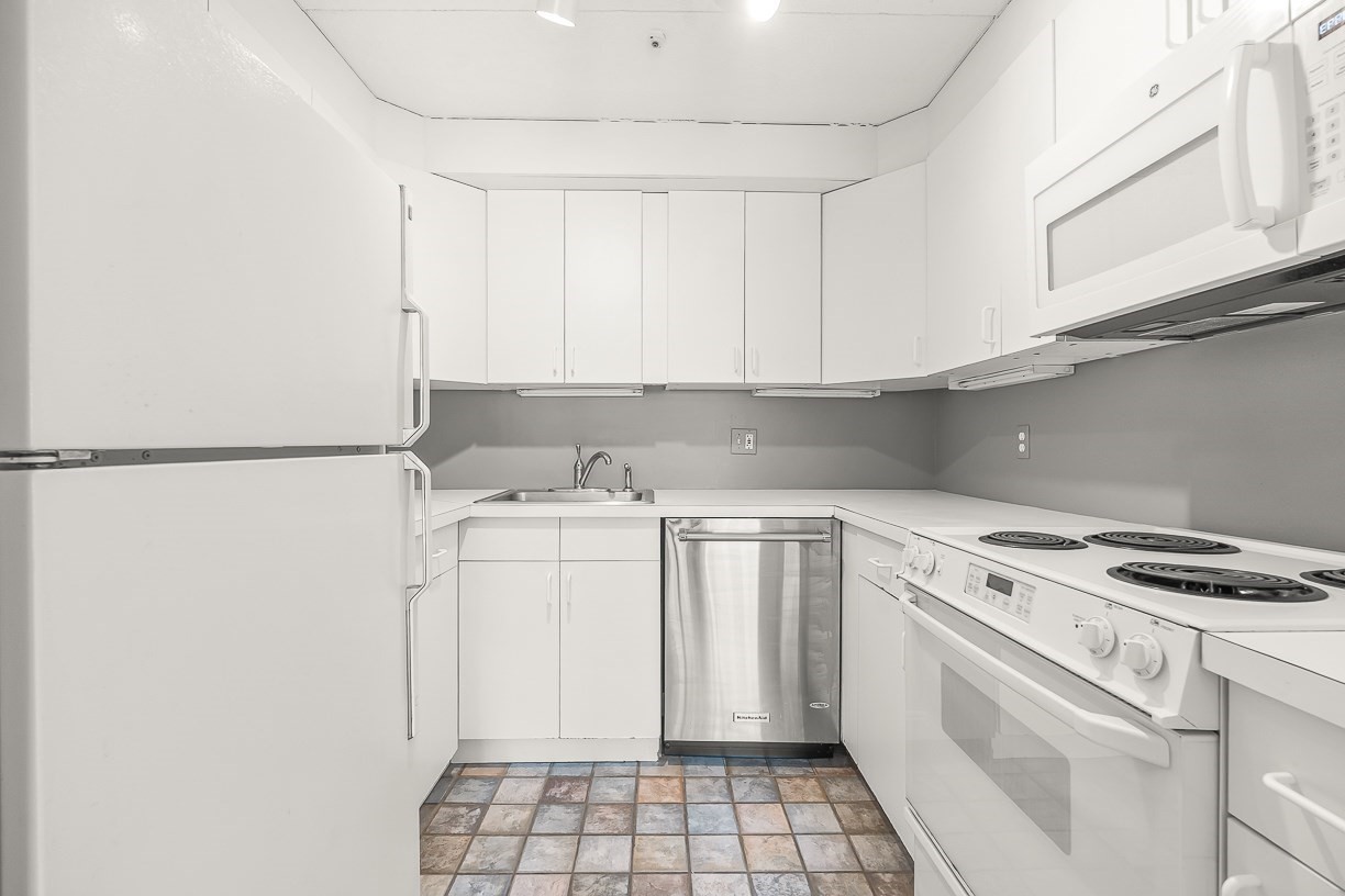 Compact U-shaped kitchen with white cabinets, stainless-steel dishwasher, and multicolored tile floor.
