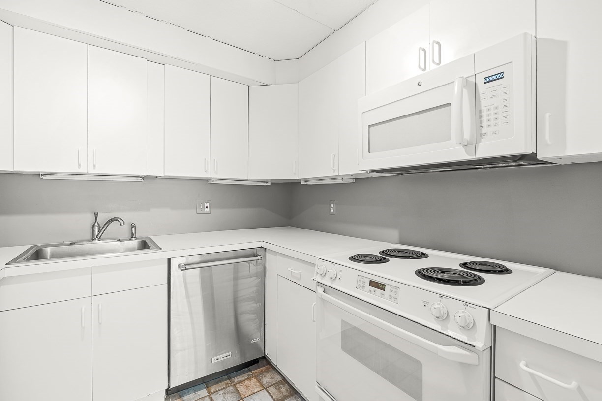 Compact white kitchen with a stainless-steel sink and dishwasher, electric range, and over-the-range microwave.